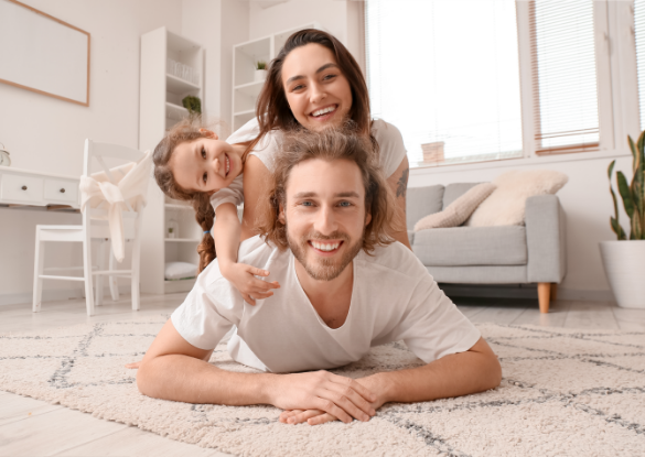 smiling father lying on floor with wife and daughter on his back