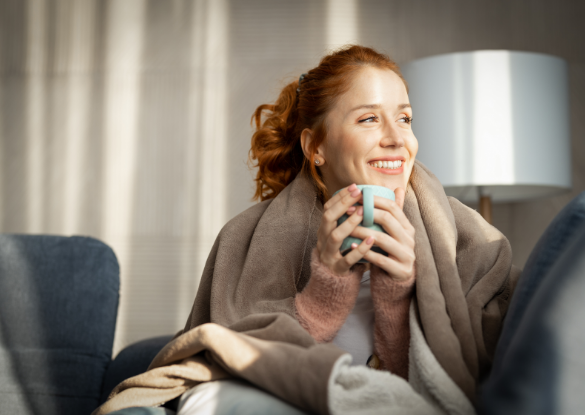 woman wrapped in blanket holding warm drink in mug with both hands