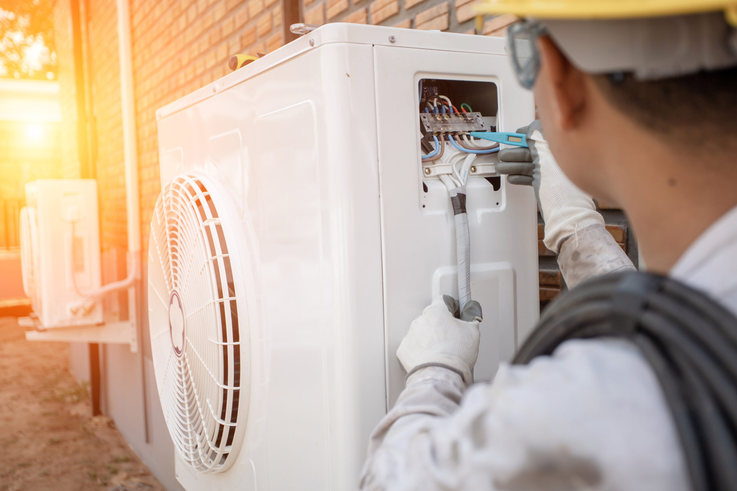 hvac technician conducting heat pump maintenance on outside unit with sunlight flare